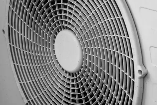 Close-up view of a circular fan grill with a grid pattern, likely part of a heat pump repair or ventilation system.